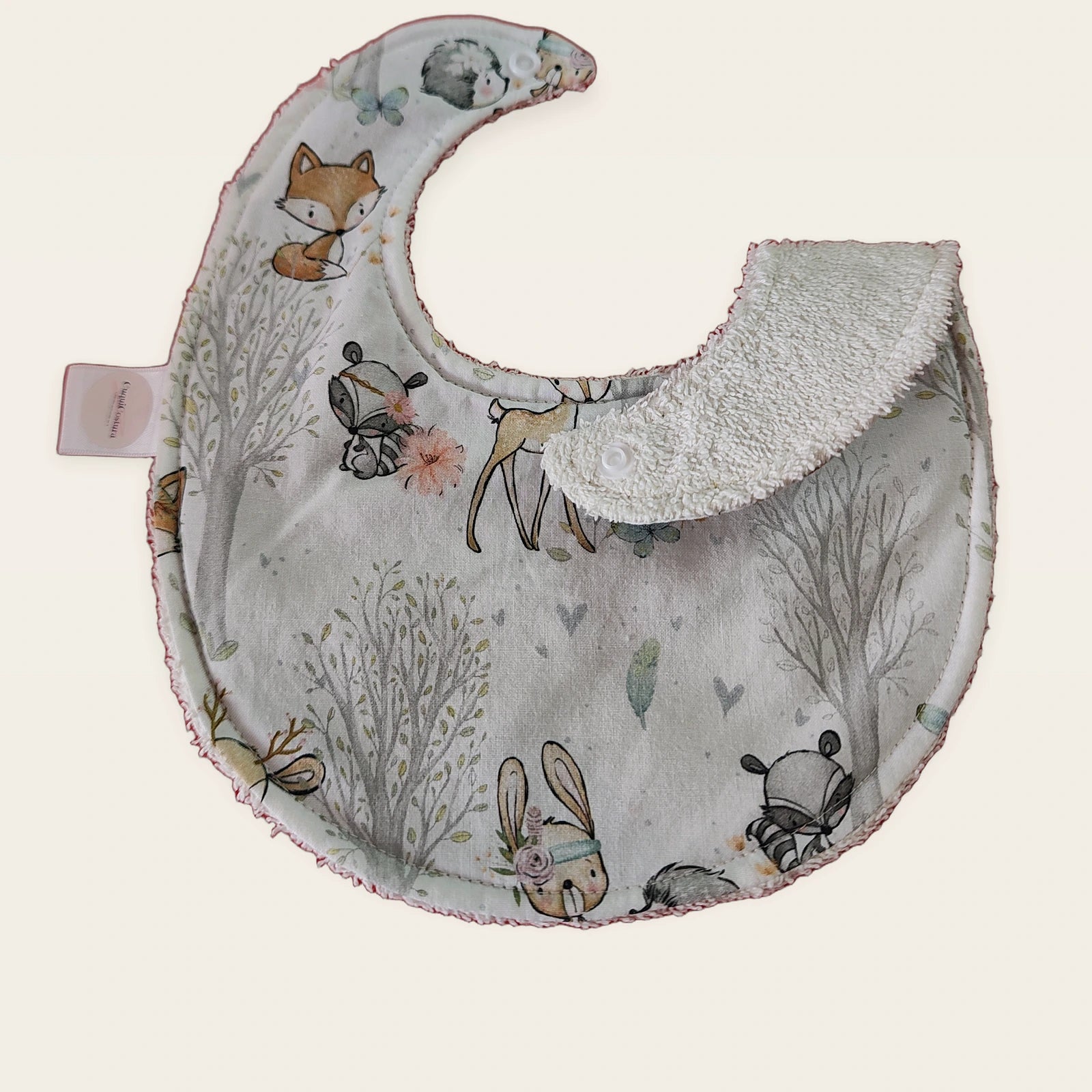 Babero impermeable 0–6 meses Bosque encantado con una pata doblada para mostrar el rizo de algodón blanco roto