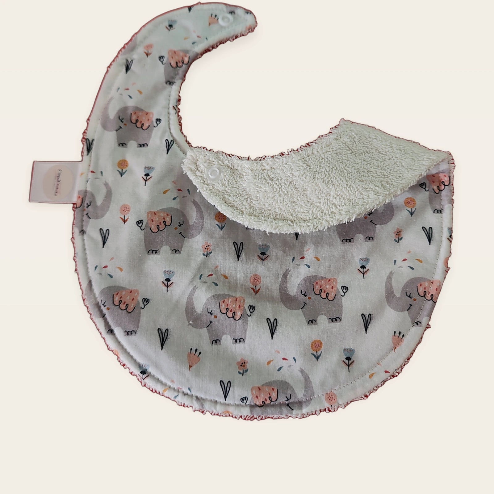 Babero impermeable 0–6 meses Cuquielefantes con una pata doblada para mostrar el rizo de algodón blanco roto