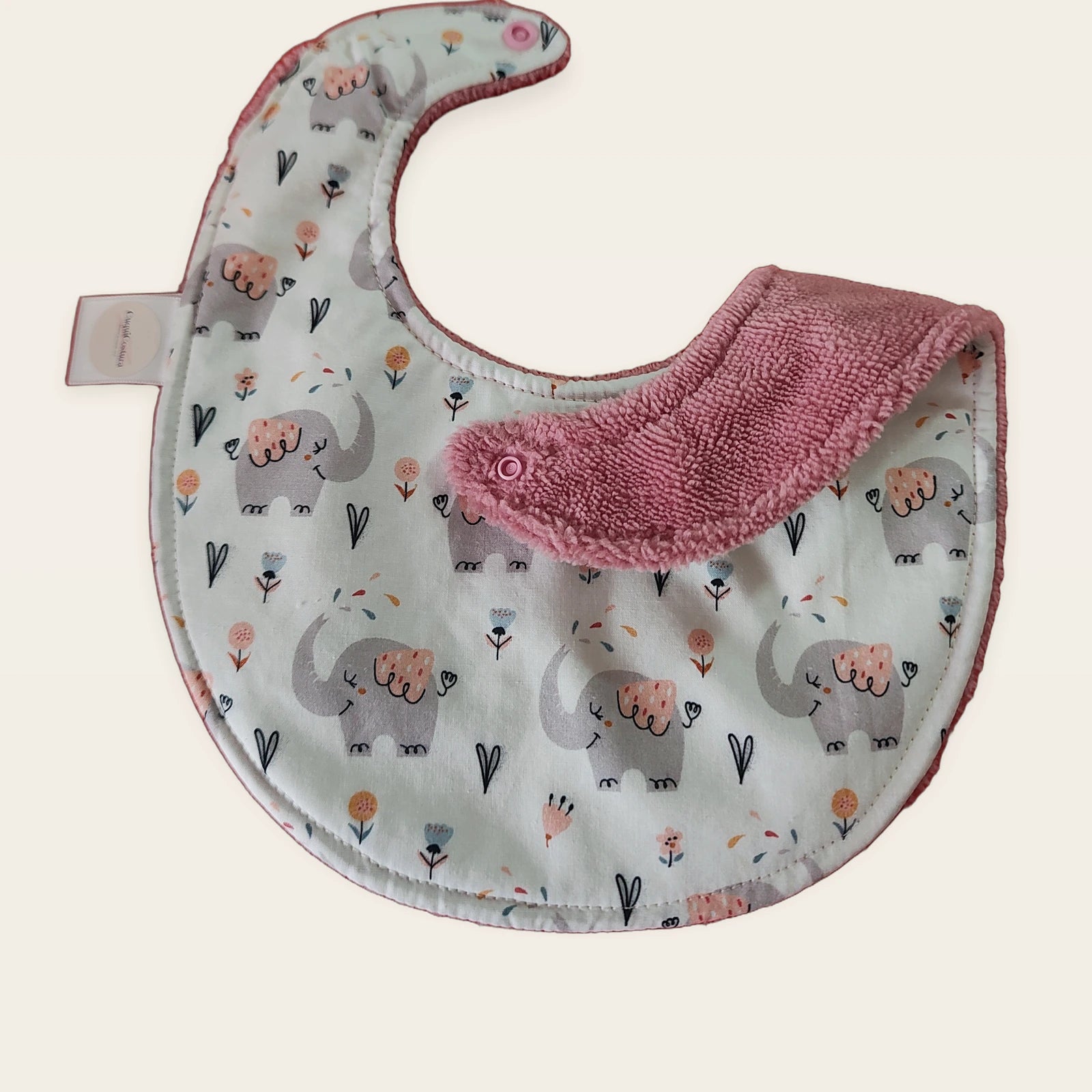 Babero impermeable 0–6 meses Cuquielefantes con una pata doblada para mostrar el rizo de bambú rosa empolvado