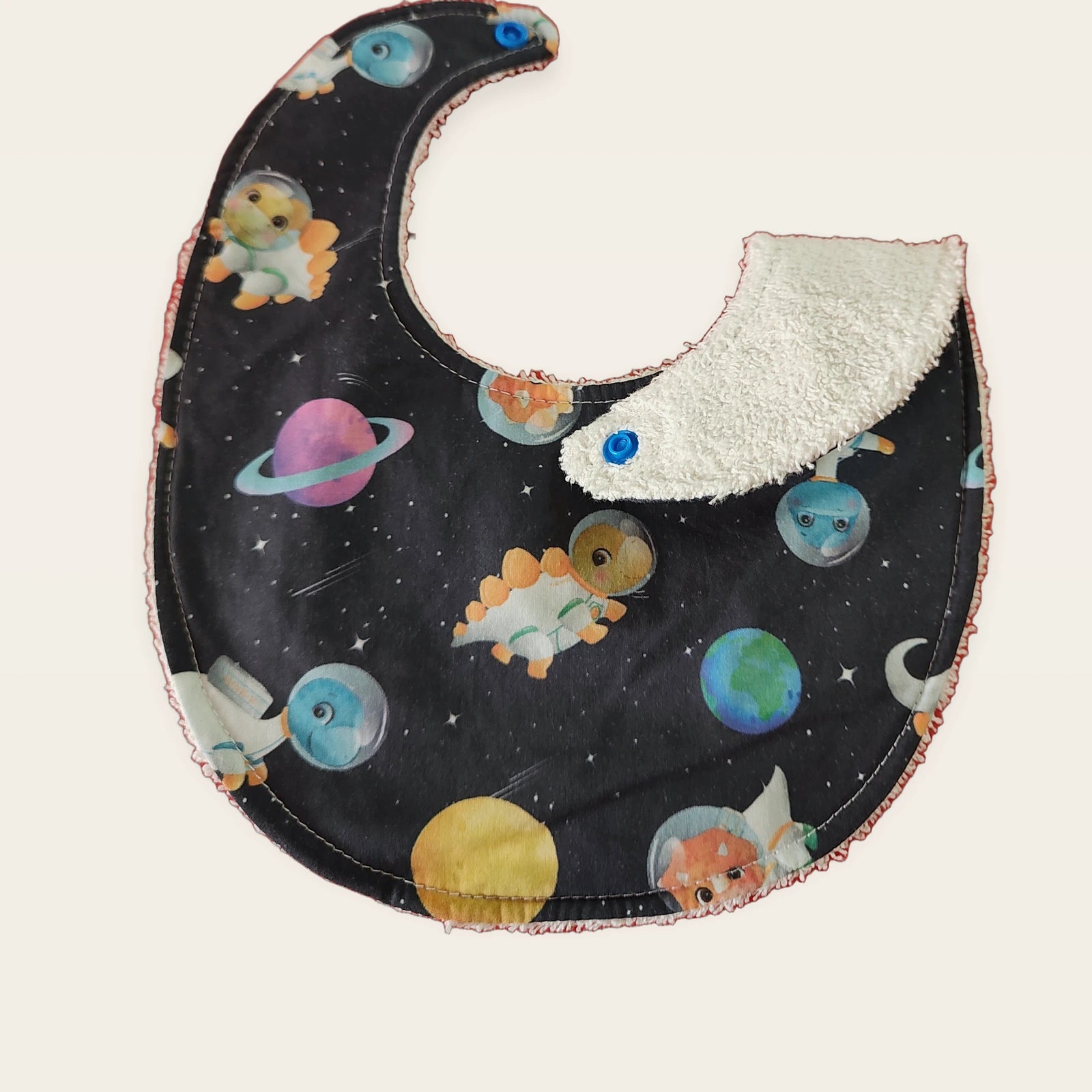 Babero impermeable 0–6 meses Dinosaurios del espacio con una pata doblada para mostrar el rizo de algodón blanco roto