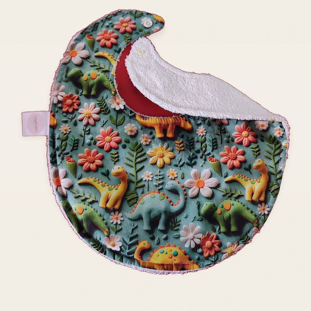 Babero impermeable 0–6 meses Dinosaurios y flores azul 3D con una pata doblada para mostrar el rizo de algodón blanco roto