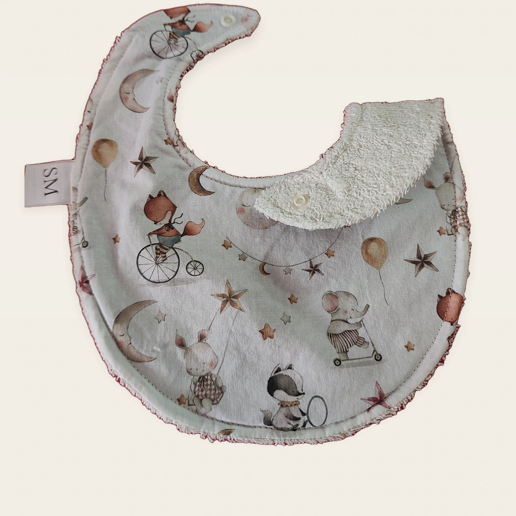 Babero impermeable 0–6 meses Elefantitos, luna y estrellas con una pata doblada para mostrar el rizo de algodón blanco roto
