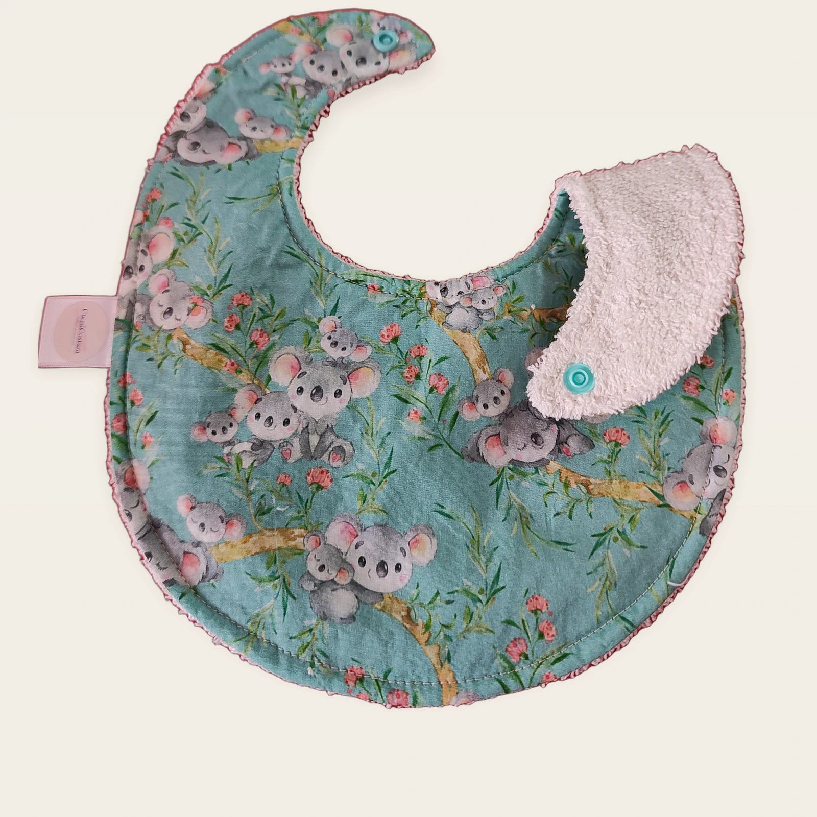 Babero impermeable 0–6 meses Koalas con una pata doblada para mostrar el rizo de algodón blanco roto