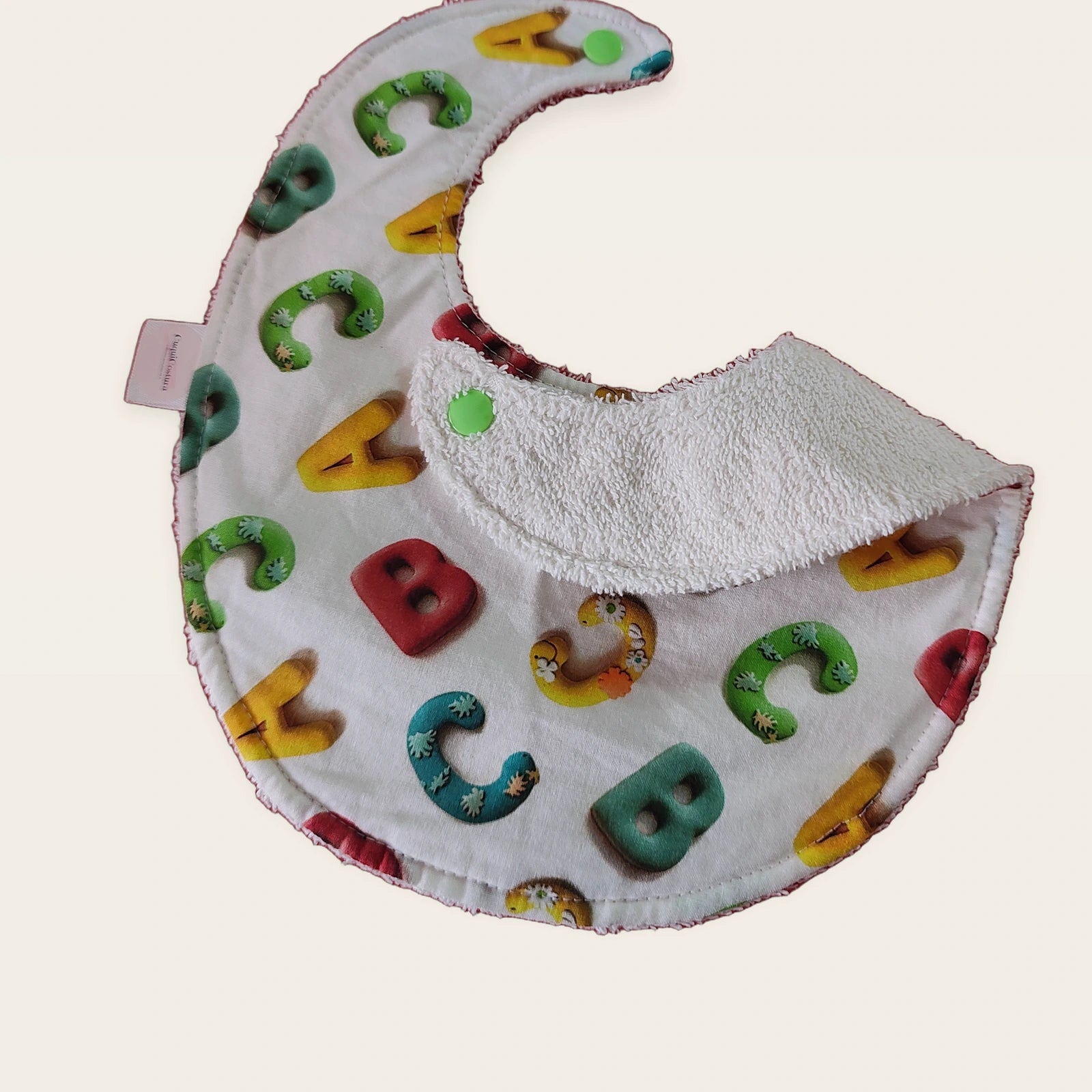 Babero impermeable 0–6 meses Letras de colores con una pata doblada para mostrar el rizo de algodón blanco roto