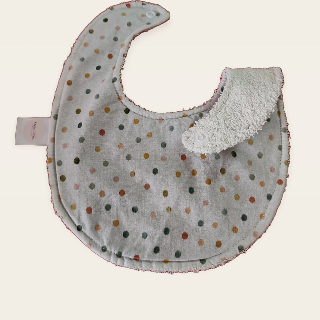 Babero impermeable 0–6 meses Lunares acuarela con una pata doblada para mostrar el rizo de algodón blanco roto