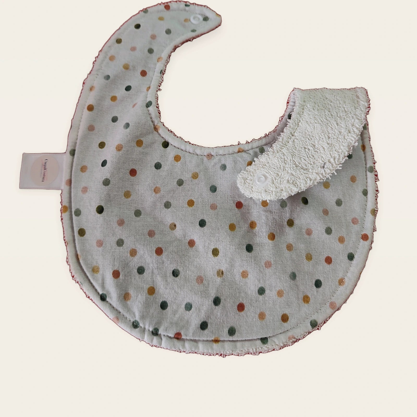 Babero impermeable 0–6 meses Lunares acuarela con una pata doblada para mostrar el rizo de algodón blanco roto