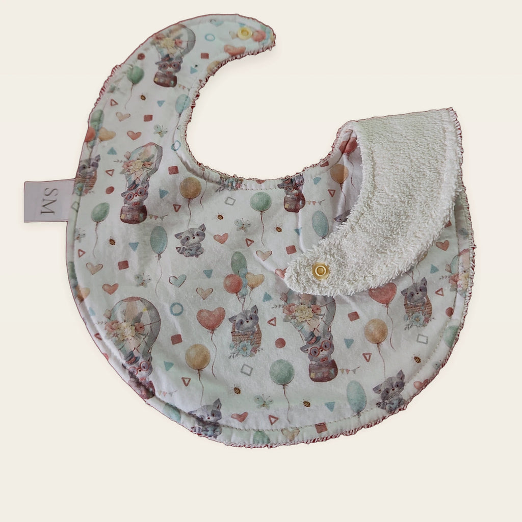 Babero impermeable 0–6 meses Mapaches con globos con una pata doblada para mostrar el rizo de algodón blanco roto