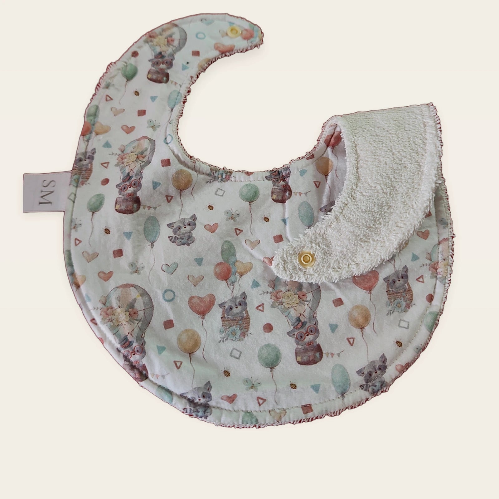 Babero impermeable 0–6 meses Mapaches con globos con una pata doblada para mostrar el rizo de algodón blanco roto