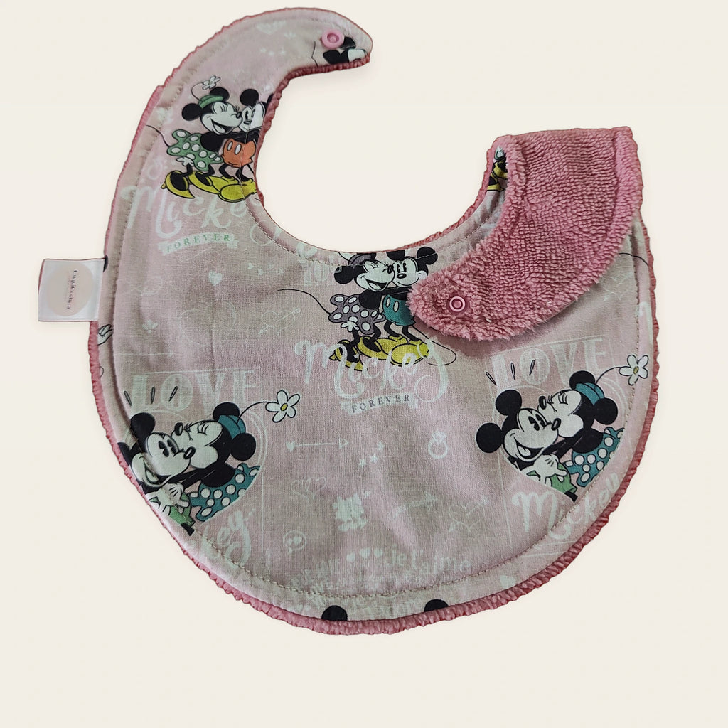 Babero impermeable 0–6 meses Mickey Forever Love con una pata doblada para mostrar el rizo de bambú rosa empolvado