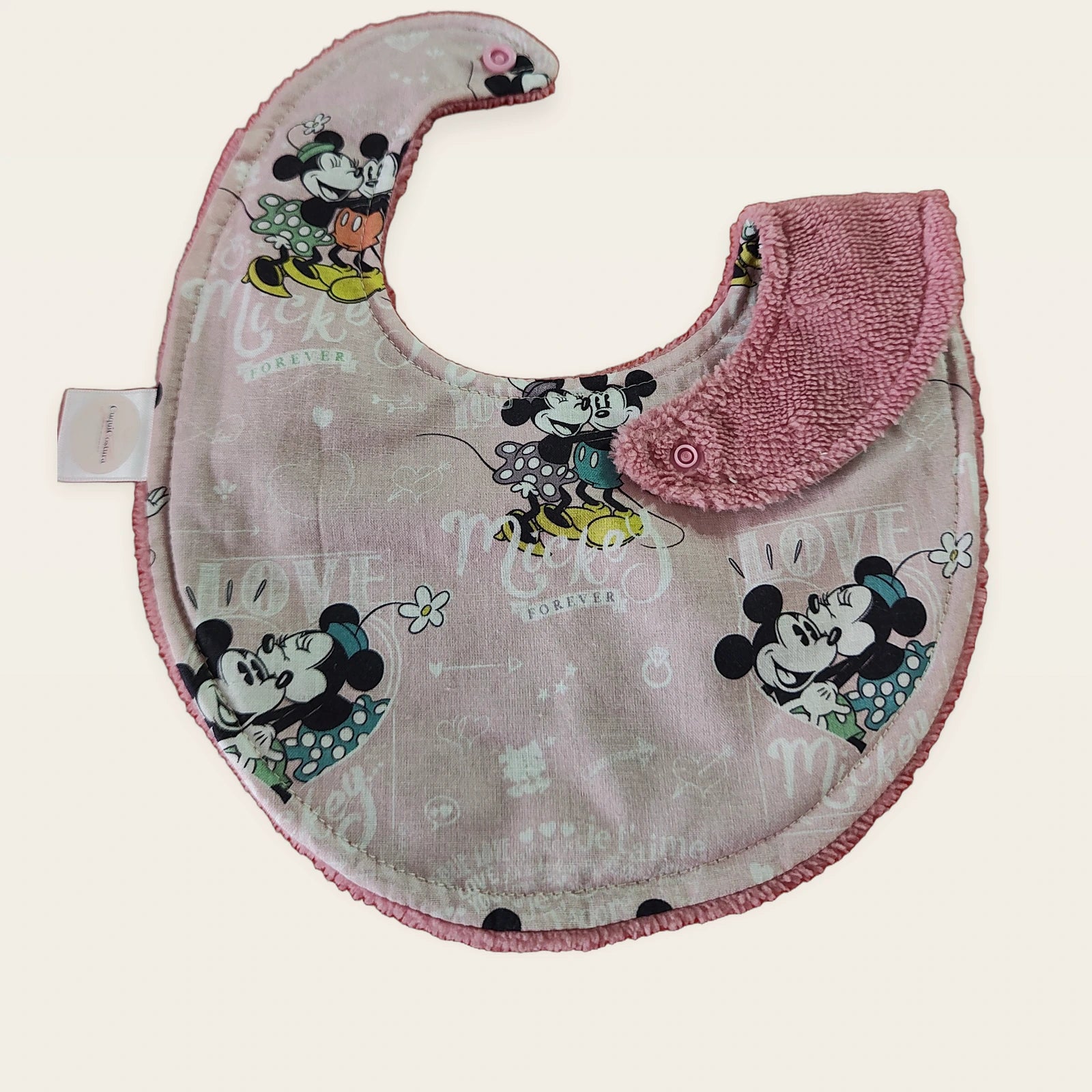Babero impermeable 0–6 meses Mickey Forever Love con una pata doblada para mostrar el rizo de bambú rosa empolvado