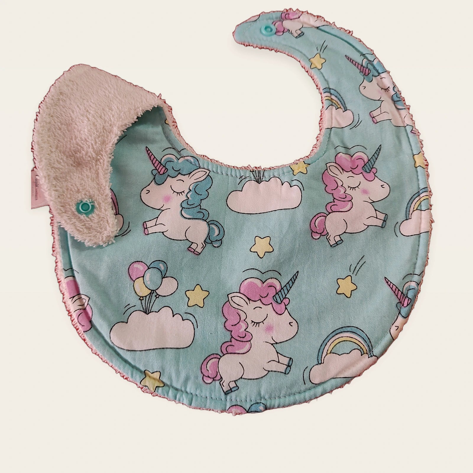 Babero impermeable 0–6 meses Unicornios entre nubes con una pata doblada para mostrar el rizo de algodón blanco roto